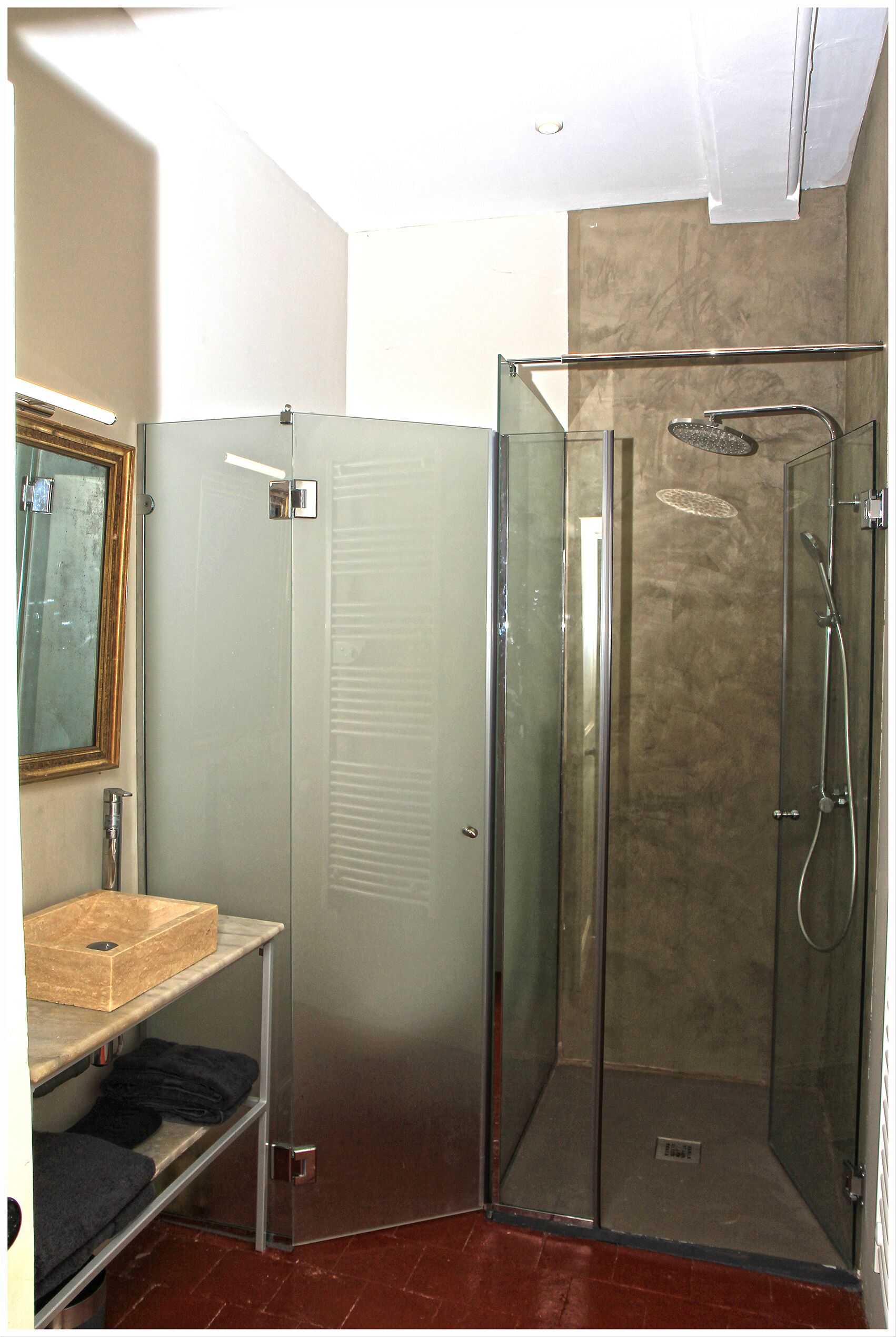A glass-enclosed shower with a handheld showerhead and a handheld faucet.