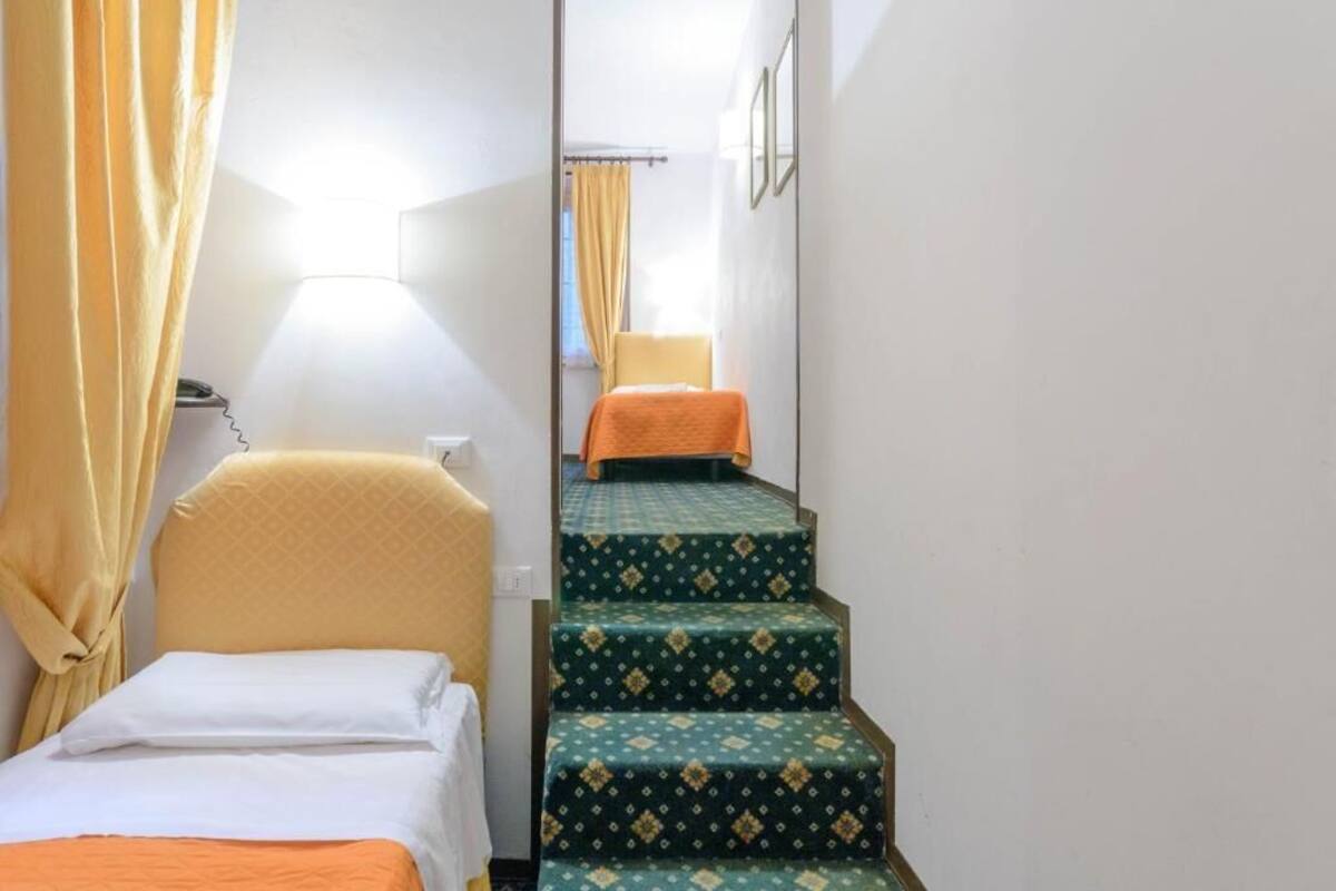 Ein schmaler Flur mit einem Bett links und einer Treppe, die zu einem anderen Raum führt.