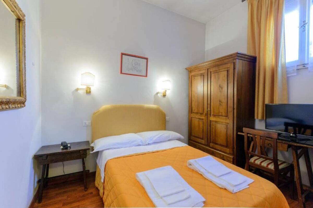 Ein Hotelzimmer mit einem Bett, einem Holzschrank, einem Schreibtisch mit Stuhl, einem Fernseher und zwei Wandleuchten.