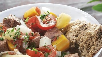 A plate of beef stew with vegetables and a slice of bread on a wooden table.