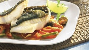 Un plato de pescado con verduras y una rodaja de lima sobre un mantel tejido.