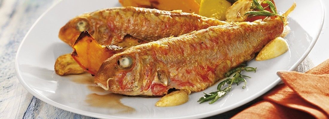 Dos peces enteros en un plato blanco con rodajas de limón y hierbas aromáticas.