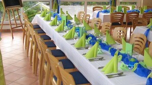 Un salón de banquetes con mesas largas dispuestas para un evento formal, con manteles y servilletas verdes y azules.