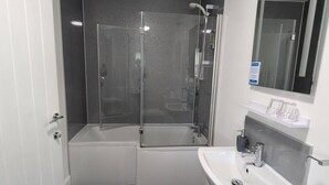A modern bathroom with a glass-enclosed shower, a white sink, and a mirror above it. - Old North Inn Hotel (Inverness)