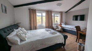 A bedroom with two beds, a TV, and a window with curtains. - Old North Inn Hotel (Inverness)