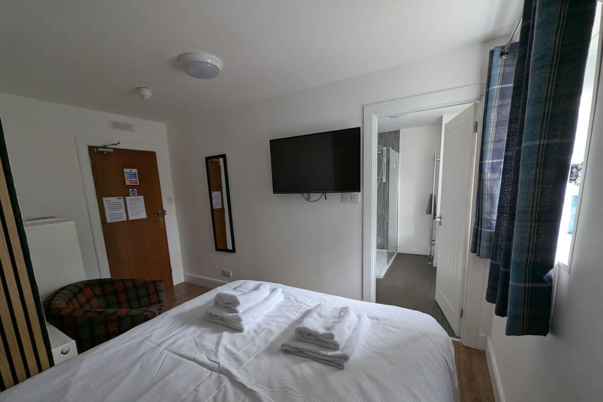 A hotel room with a bed, a flat-screen TV, a mirror, and a door leading to a bathroom.