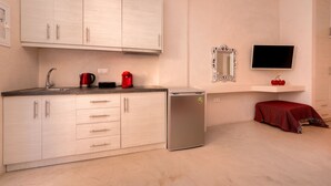 Une cuisine compacte équipée d’un réfrigérateur, d’un évier et d’un four à micro-ondes. On y trouve une petite table recouverte d’une nappe rouge et un miroir au-dessus.