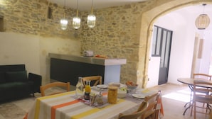 A dining area with a stone wall, a table set with a striped tablecloth, and a stone fireplace. - Maison d'hôtes la Bignone (Laudun)