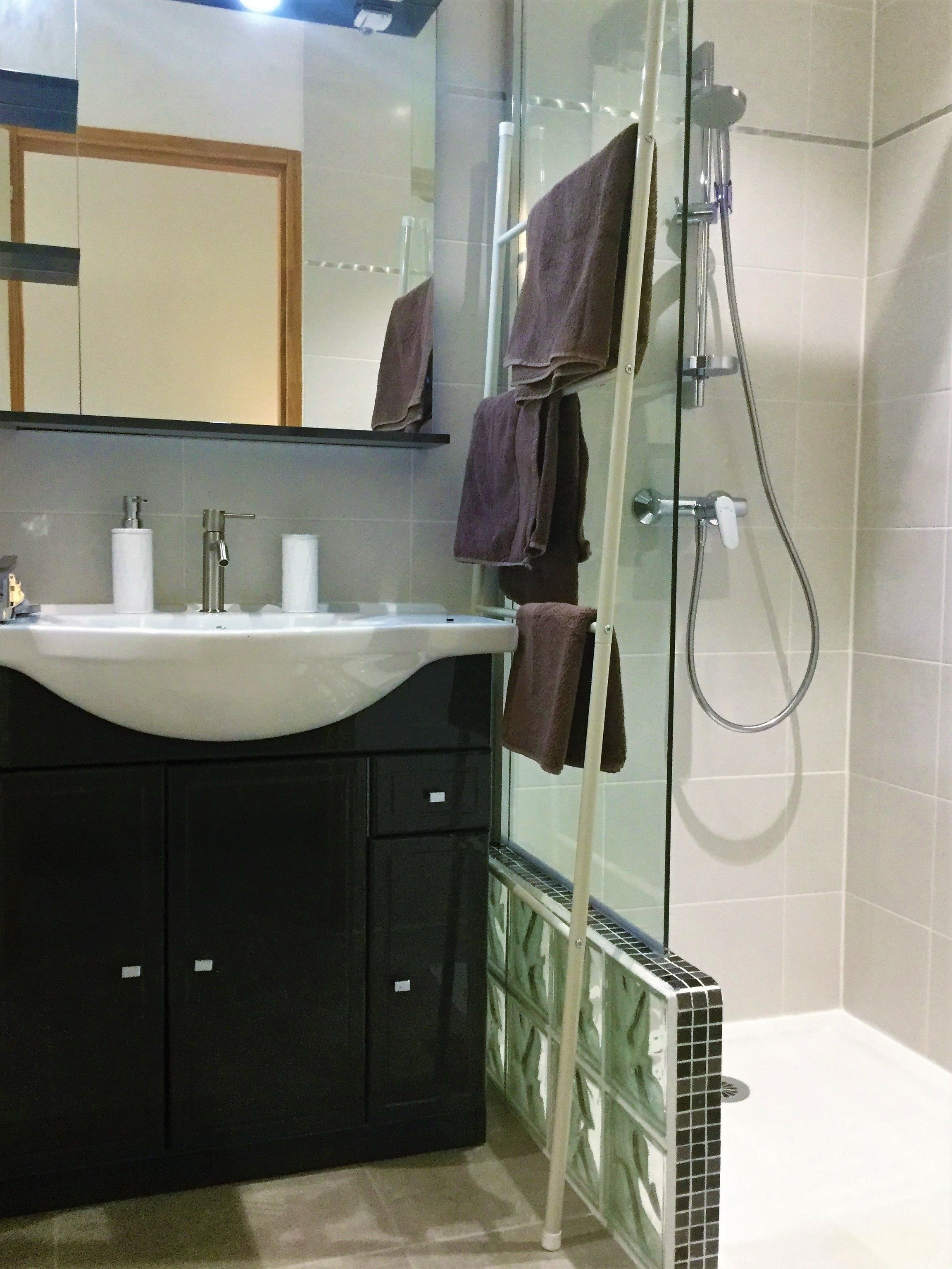 Een badkamer met een douchecabine van glas, een wastafel met spiegel erboven en handdoeken aan de douchedeur.