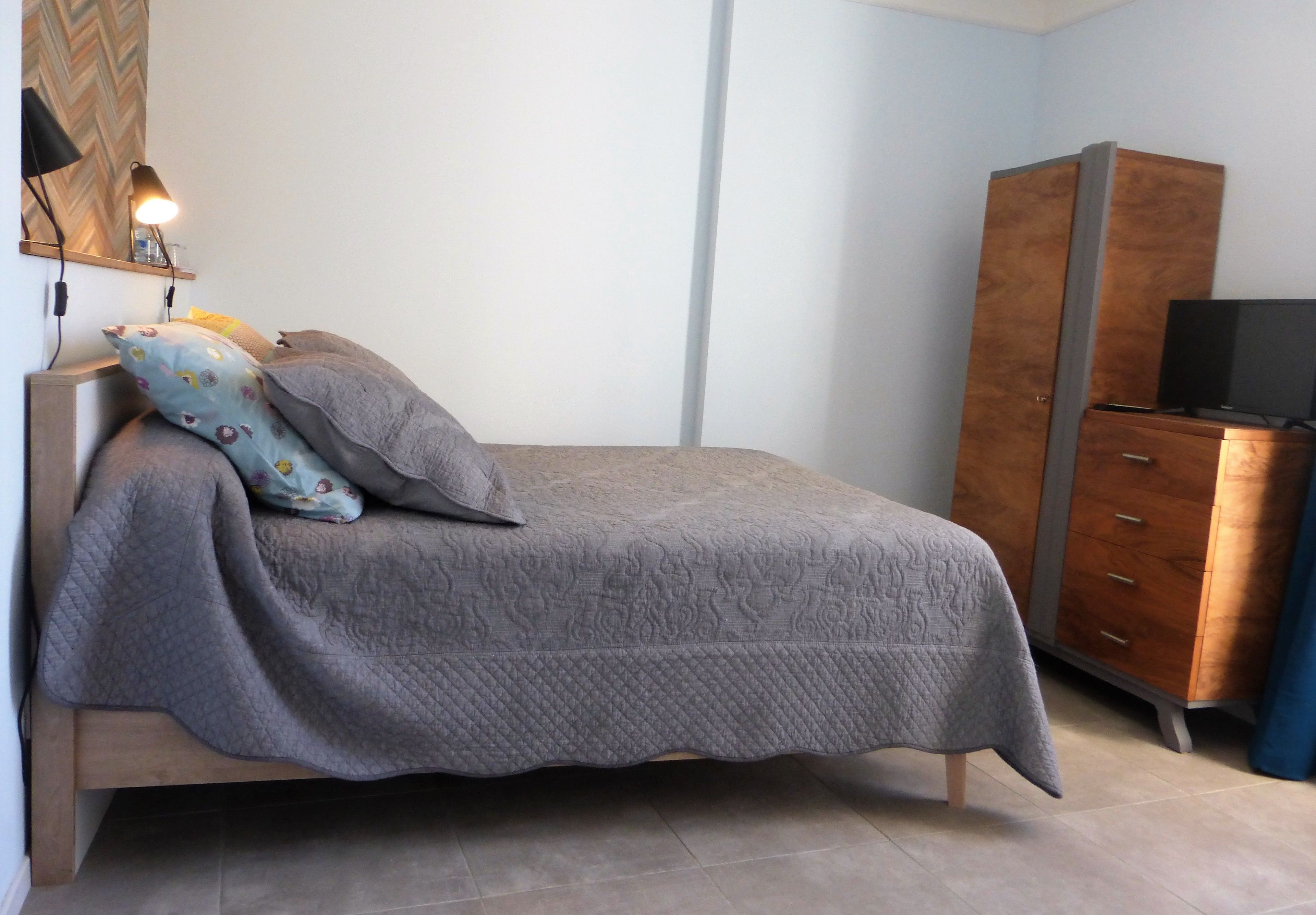 A bedroom with a bed, a nightstand, a lamp, a wardrobe, and a television.