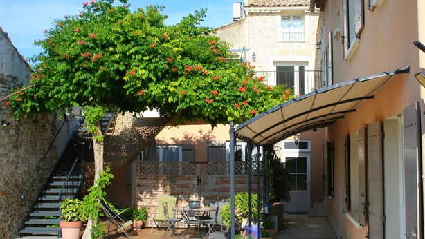 A courtyard with a pergola covered patio, outdoor seating, and potted plants. - Maison d'hôtes la Bignone (Laudun)