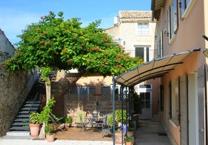A courtyard with a pergola covered patio, outdoor seating, and potted plants. - Maison d'hôtes la Bignone (Laudun)