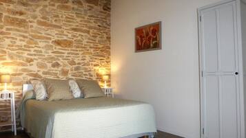 A bedroom with a stone wall, a bed with a quilt, two bedside lamps, and a white wardrobe.