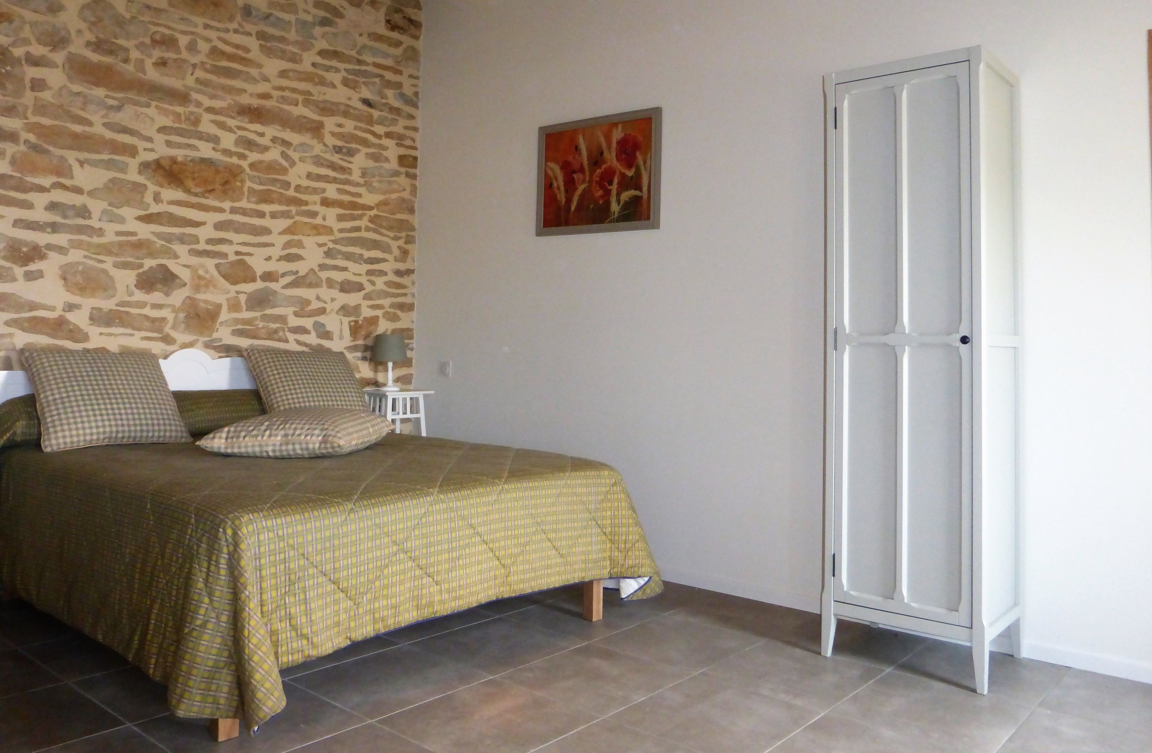 Une chambre à coucher avec un lit, une table de chevet, une lampe, une armoire et un mur en pierre.