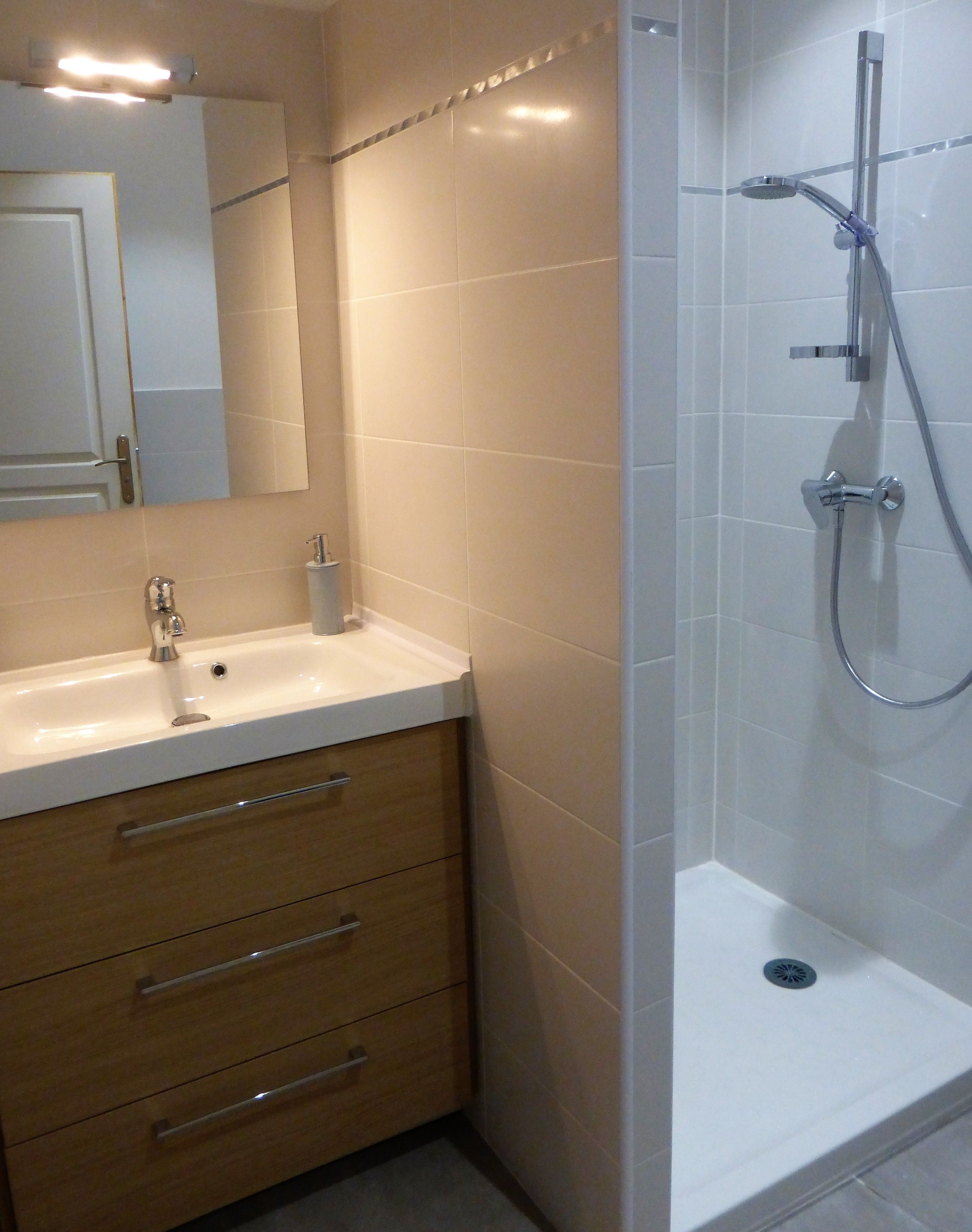 Un baño moderno con lavamanos blanco, mueble de madera y zona de ducha con mampara de vidrio.