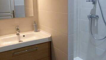 Un baño moderno con lavamanos blanco, mueble de madera y zona de ducha con mampara de vidrio.