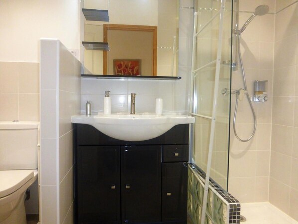 A bathroom with a white sink, black cabinets, a glass shower enclosure, and a toilet. - Maison d'hôtes la Bignone (Laudun)