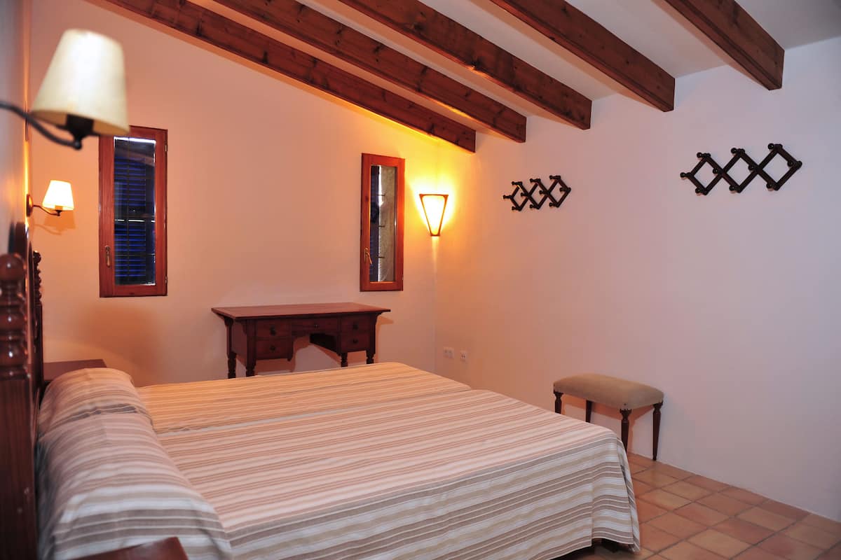 A bedroom with a bed, bedside lamps, a wooden bench, a mirror, and wall-mounted decorations.