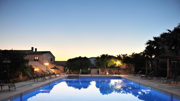 A swimming pool with lounge chairs and a stone building in the background. - Finca Ses Cases Noves (Sant Llorenc des Cardassar)