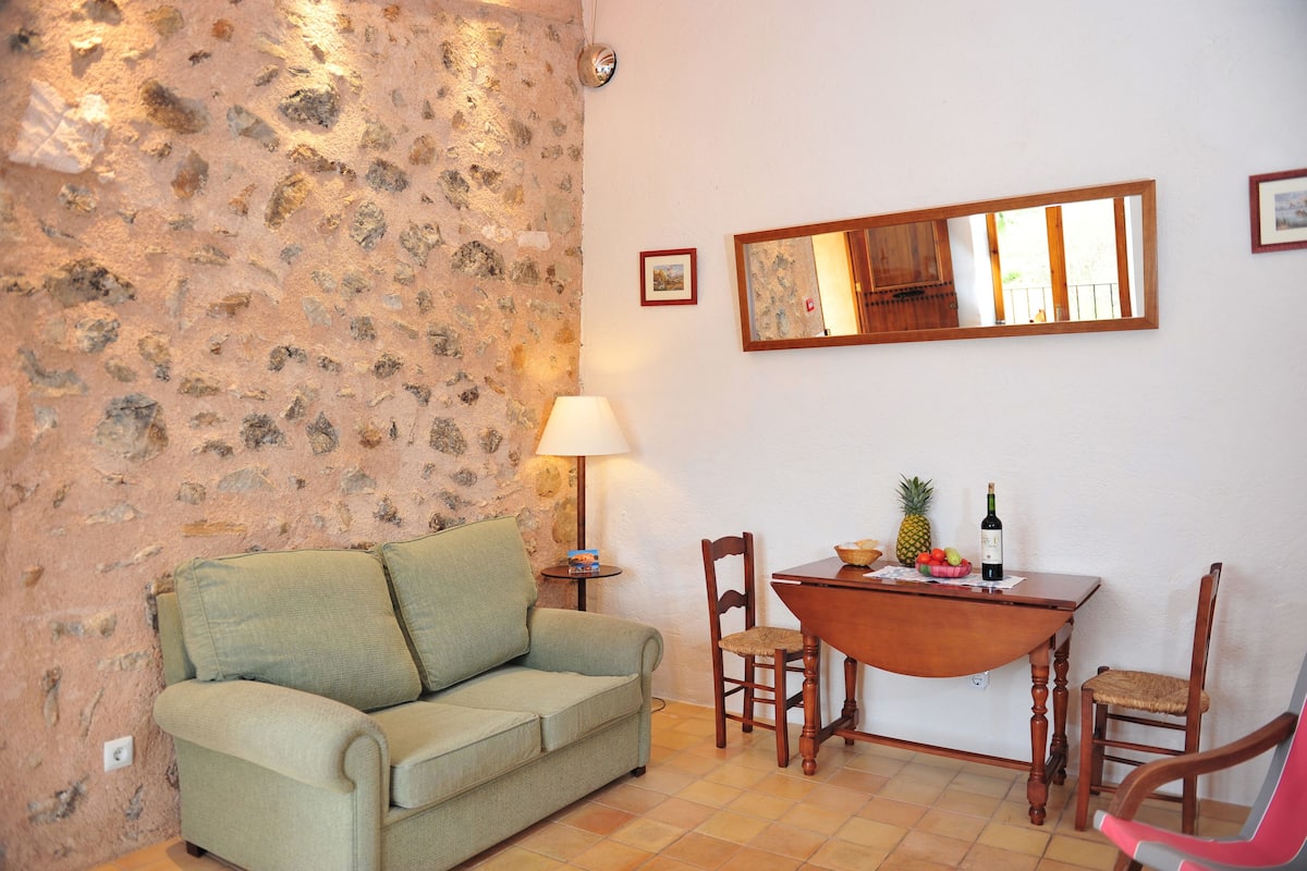 A living room with a stone wall, a sofa, a dining table with chairs, a lamp, and a mirror.
