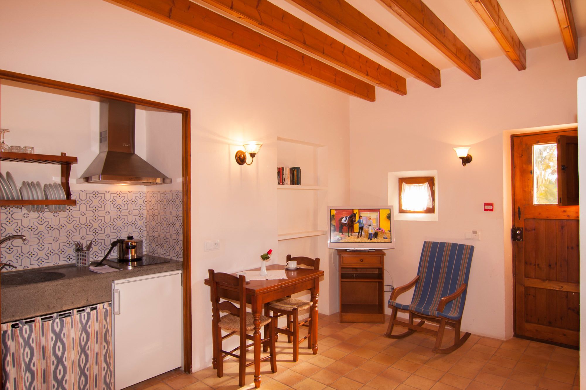 Une cuisine compacte dotée d’une cuisinière intégrée, d’un coin repas avec des chaises en bois et d’un téléviseur posé sur un meuble en bois.