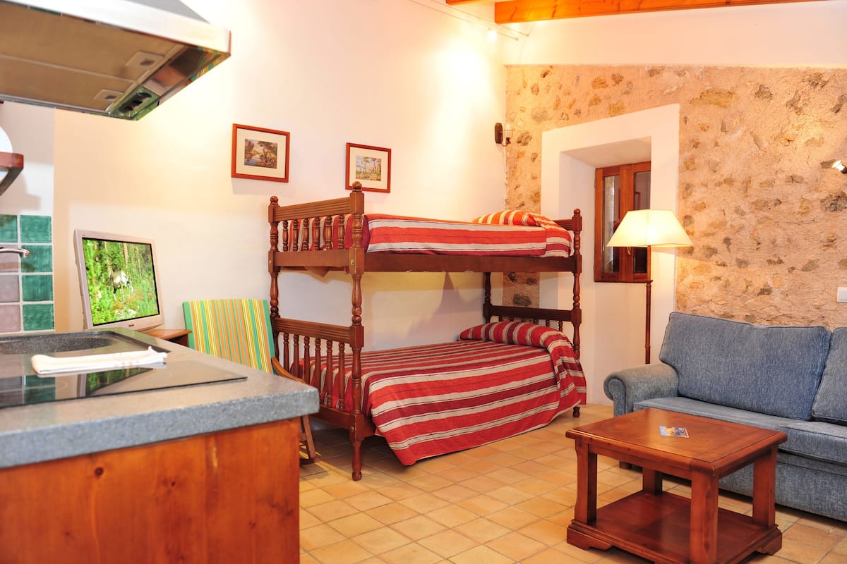 A bunk bed with a red and white striped bedspread, a wooden nightstand, a blue sofa, and a small wooden table.