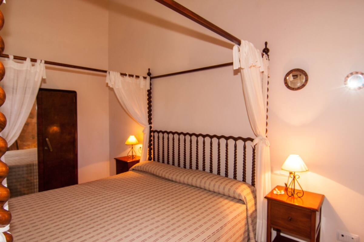 A four-poster bed with a wooden headboard, two bedside tables with lamps, and a mirror on the wall.