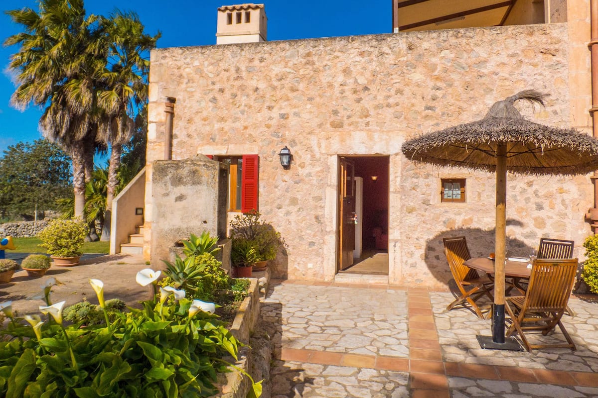 A stone building with a thatched umbrella, outdoor seating, and potted plants.