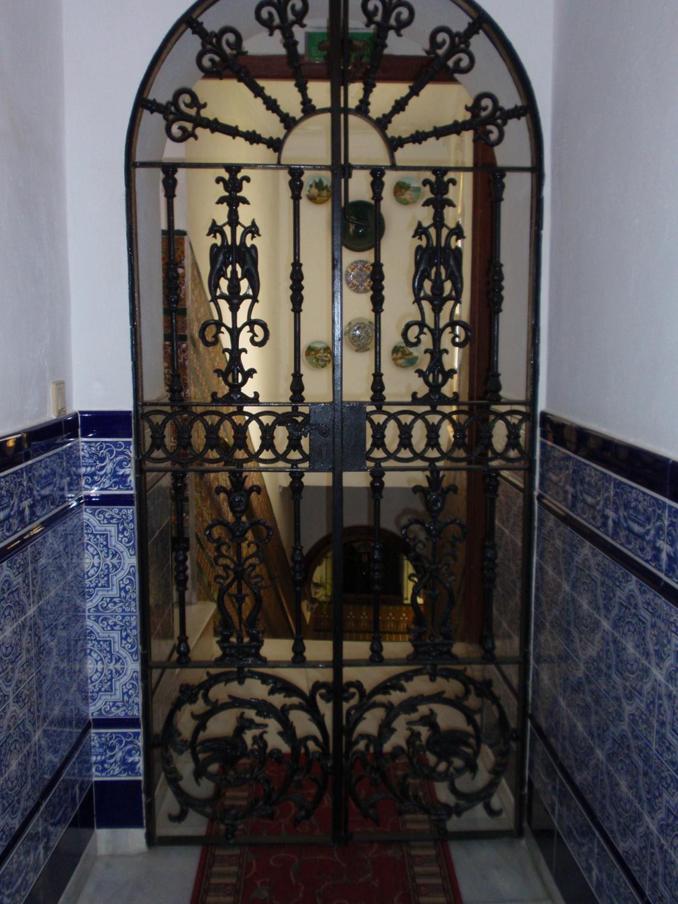 Un pasillo con una reja de hierro decorativa, baldosas azules con un estampado y una alfombra roja.