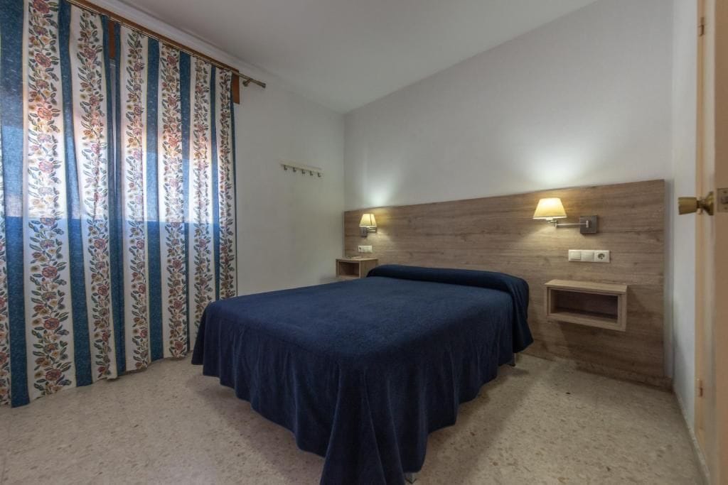 Une chambre à coucher avec un lit, deux lampes de chevet, une tête de lit en bois et un rideau à motifs floraux.