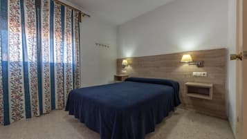Un dormitorio con cama, dos lámparas de noche, cabecera de madera y cortina con estampado floral.
