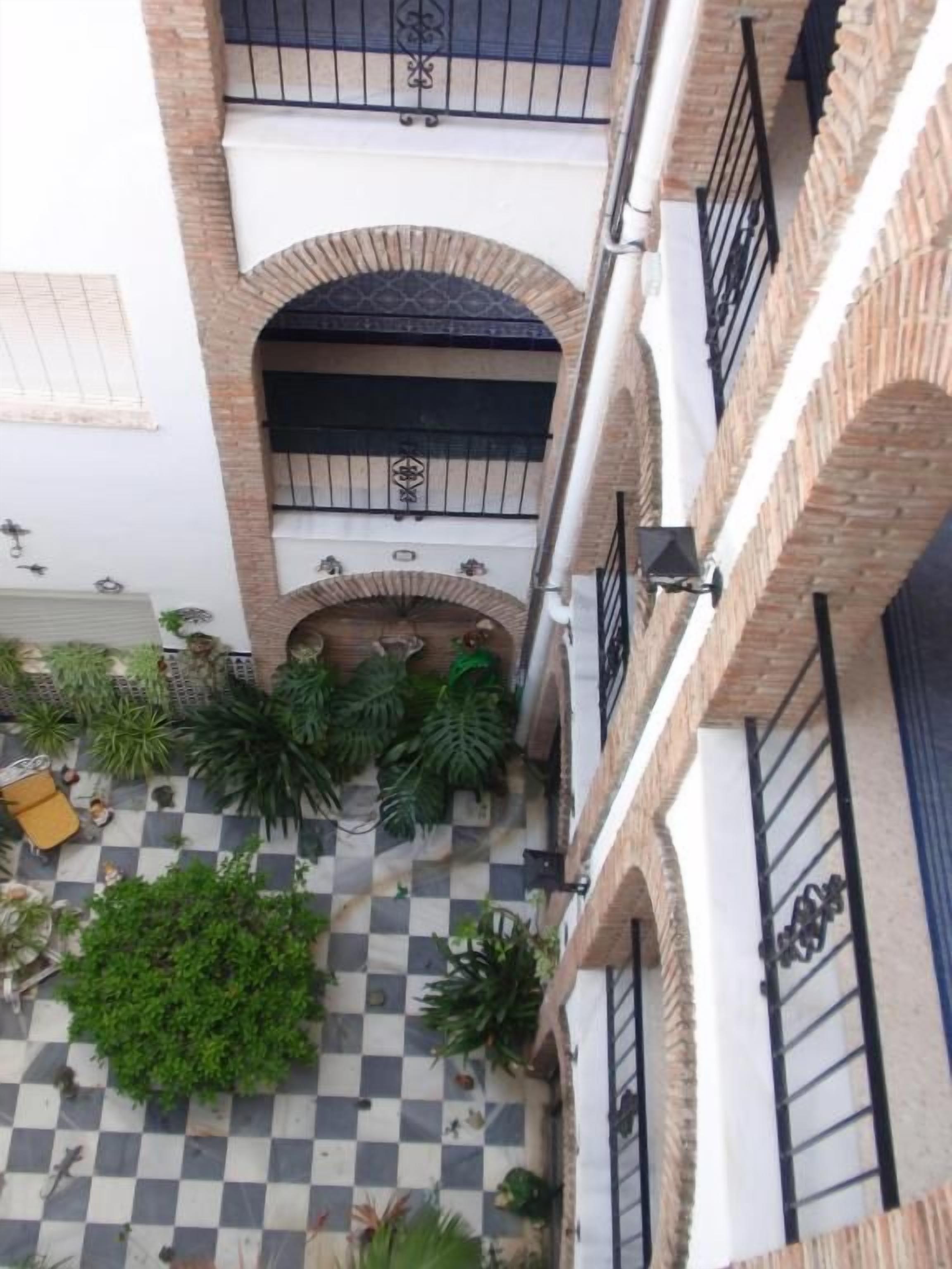 An aerial view of a courtyard with a checkered floor, surrounded by brick walls and balconies with black railings.