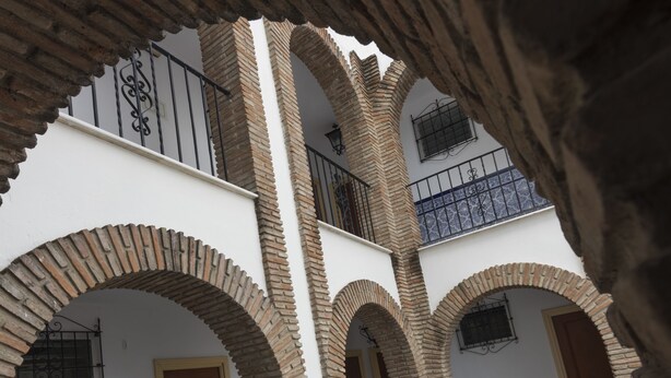 Un patio con varios arcos, una puerta de madera y paredes con azulejos.