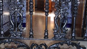 Una elaborada puerta de hierro forjado con diseños intrincados, que da paso a un pasillo con paredes de azulejos y suelo de madera.