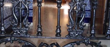 Una elaborada puerta de hierro forjado con diseños intrincados, que da paso a un pasillo con paredes de azulejos y suelo de madera.