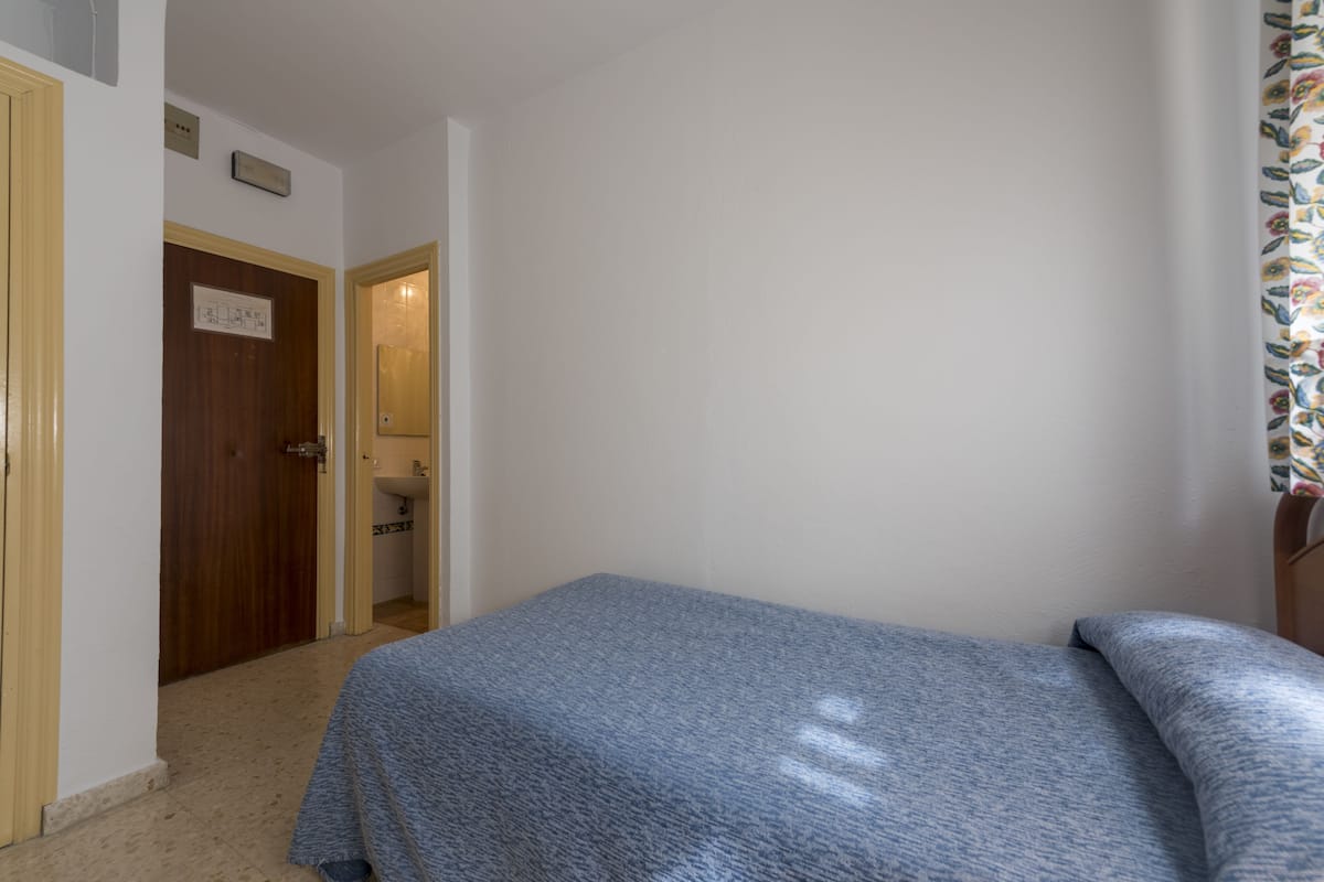 Een slaapkamer met een bed, een houten deur en een zichtbare badkamer door een open doorgang.