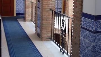 Un couloir avec des arches en briques, un sol à motifs bleus et une porte au fond.