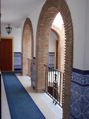 Un pasillo con arcos de ladrillo, suelo estampado en azul y una puerta al final.