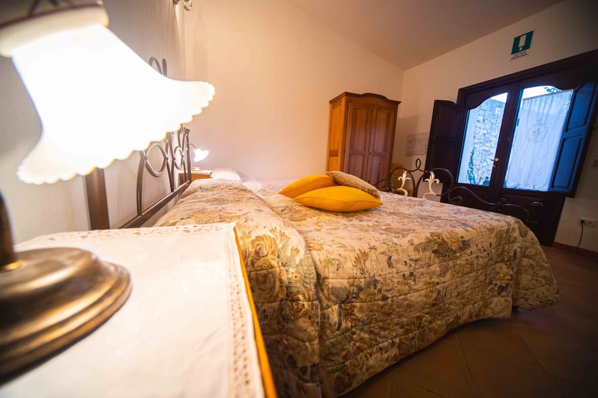 A bedroom with a bed, a lamp, a wooden wardrobe, and a window with curtains.