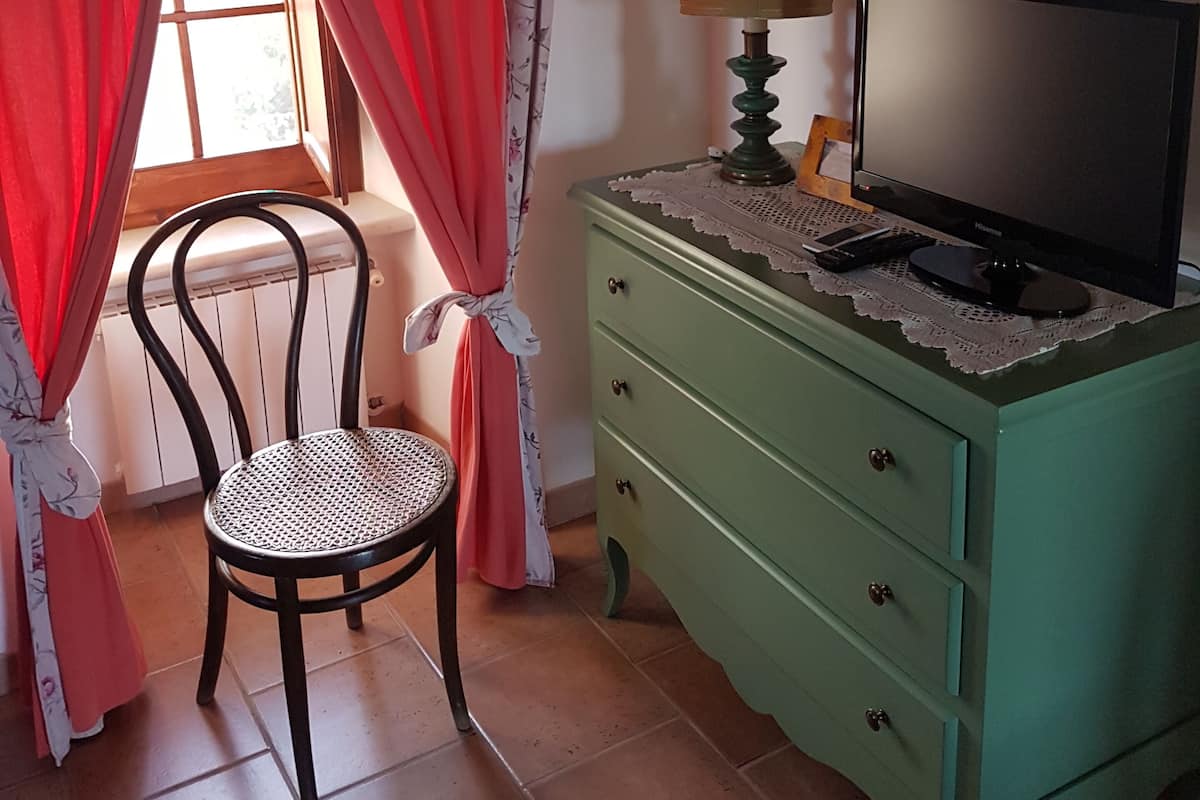 A room with a chair, a green dresser, a television, and a window with red curtains.