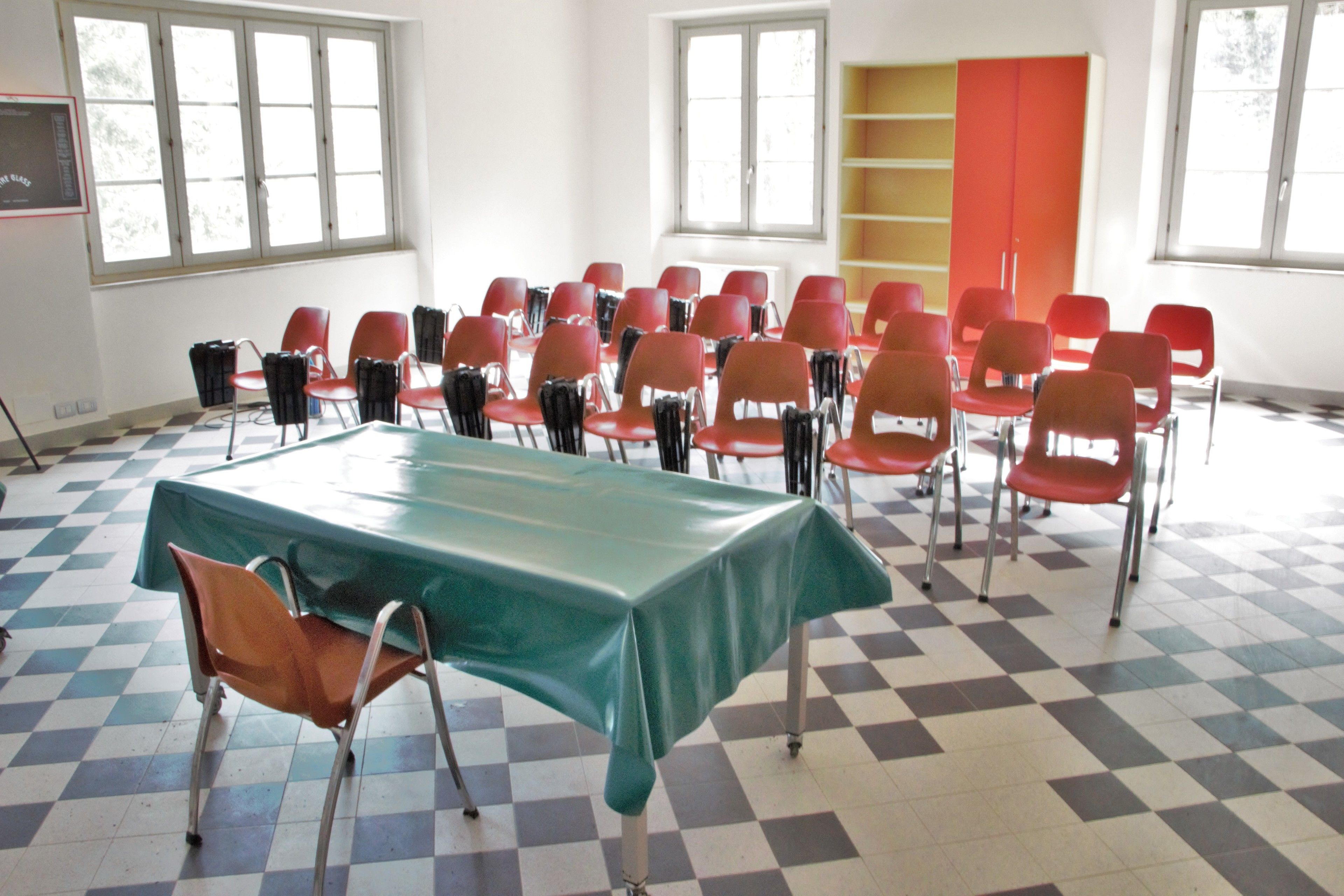A conference room with a checkered floor, a green table, and red chairs.