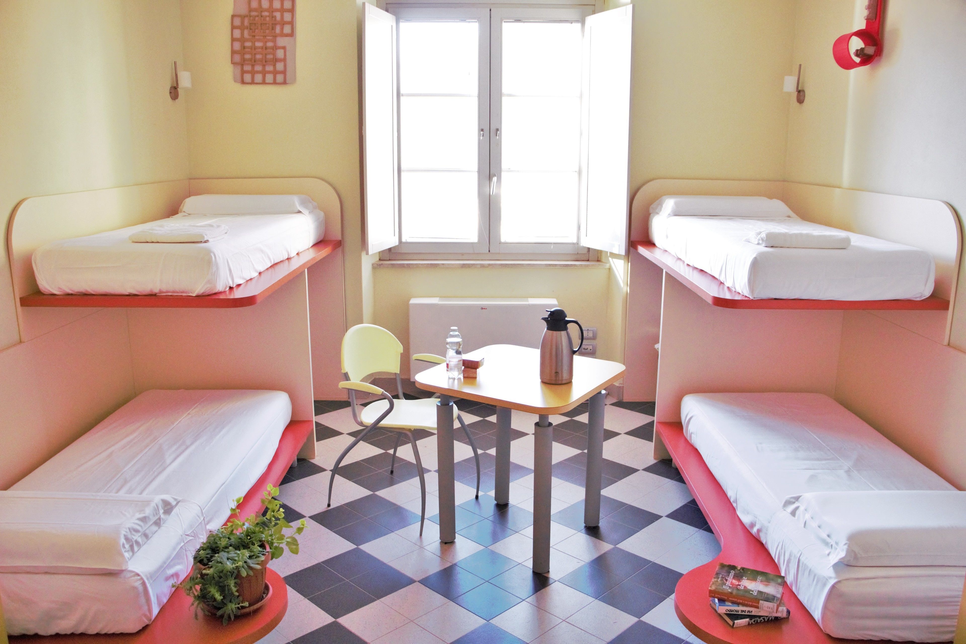 A room with bunk beds, a small table with a kettle, a chair, and a radiator.