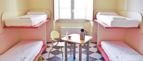 A room with bunk beds, a small table with a kettle, a chair, and a radiator.
