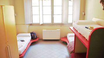 Une chambre de dortoir avec deux lits simples, un radiateur et une fenêtre dont les volets sont ouverts.