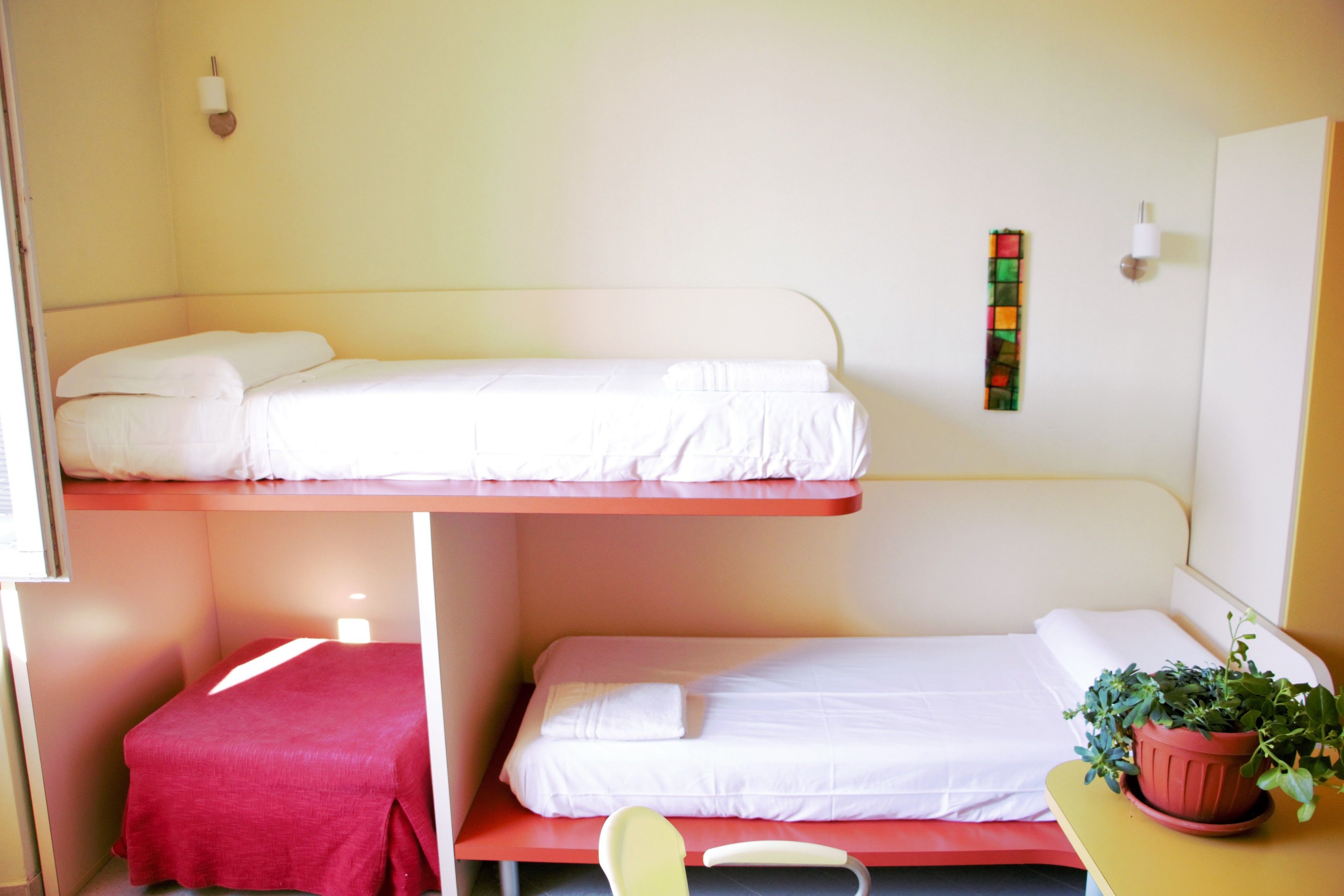 Un dormitorio con dos literas, un escritorio pequeño, una silla y una planta en maceta.