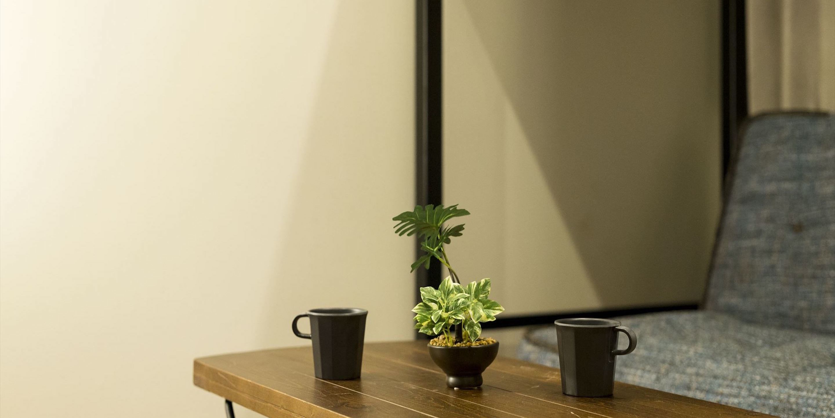 A wooden table with two black mugs and a small potted plant.