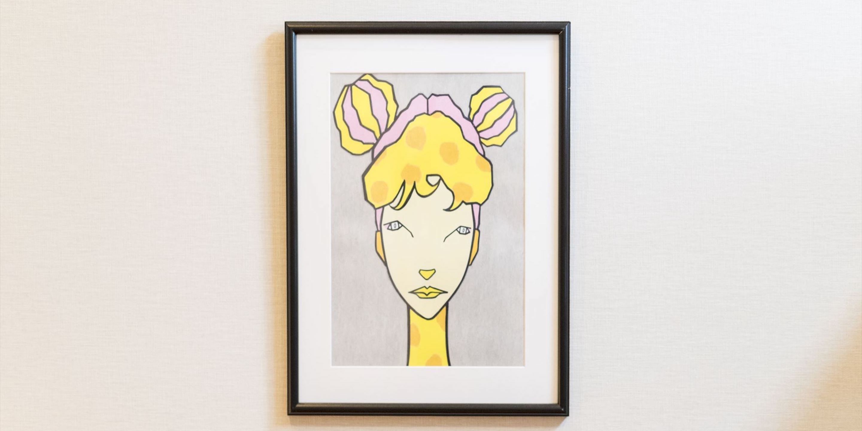 Une œuvre d’art encadrée représentant une figure stylisée avec une tête jaune et des oreilles roses.