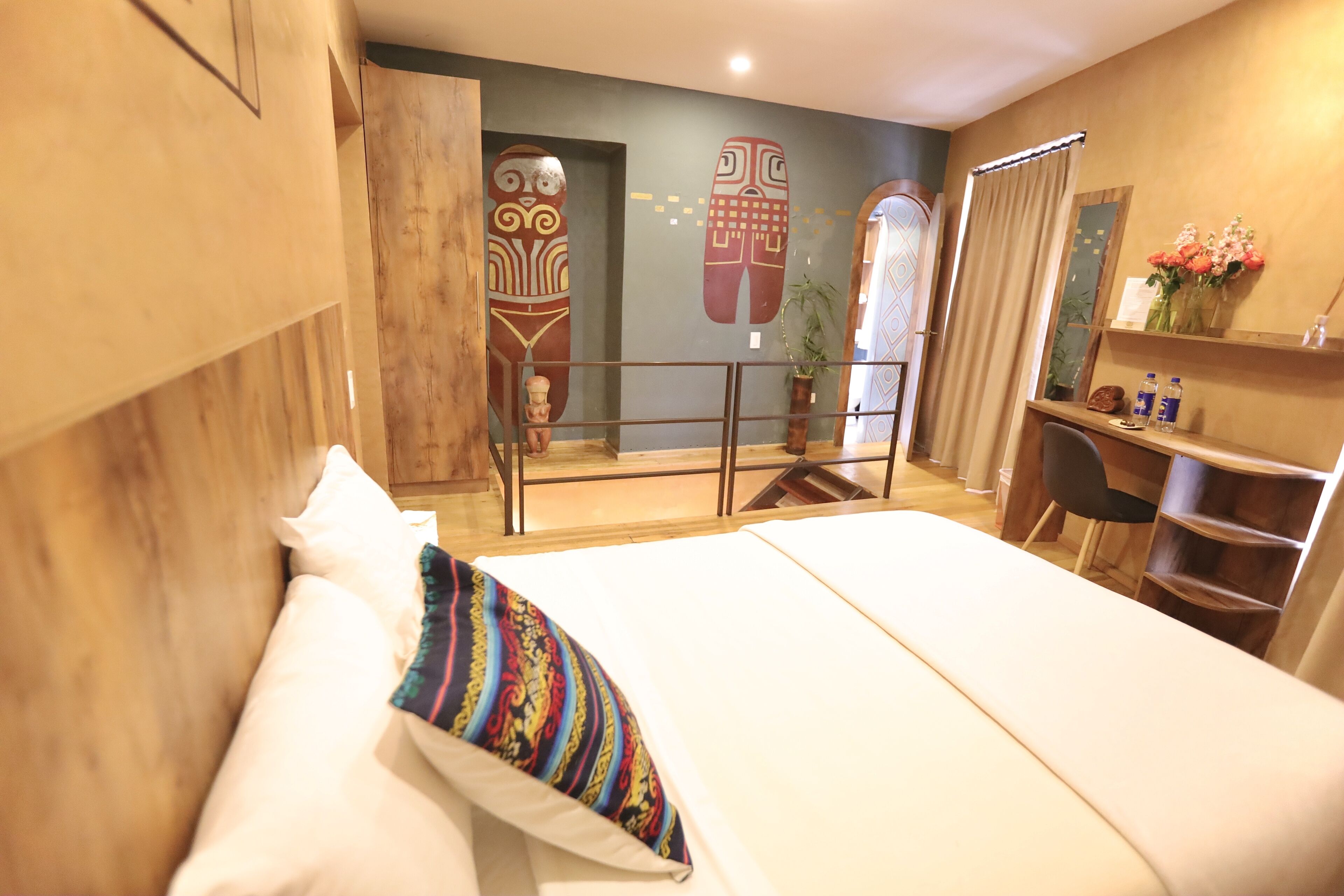 Una habitación de hotel con cama, escritorio, silla, planta pequeña y espejo.
