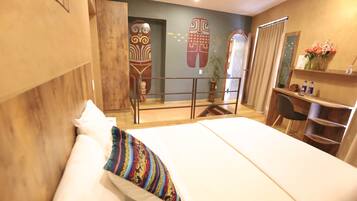 Una habitación de hotel con cama, escritorio, silla, planta pequeña y espejo.