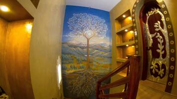 Una escalera con un mural de un árbol con raíces, barandilla de madera y una puerta decorativa con diseño metálico.